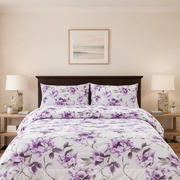 Bedroom with a bed covered in purple floral bedding, two nightstands with lamps, and a framed picture on the wall.