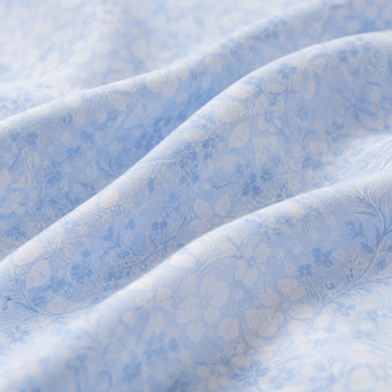 Blue floral bedspread set on a bed in a bedroom with nightstands and lamps.