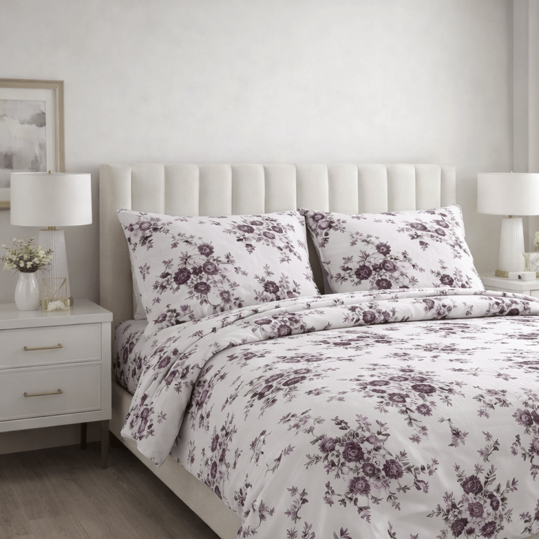 Floral bedding set on a bed in a bedroom with white walls and wooden floors.