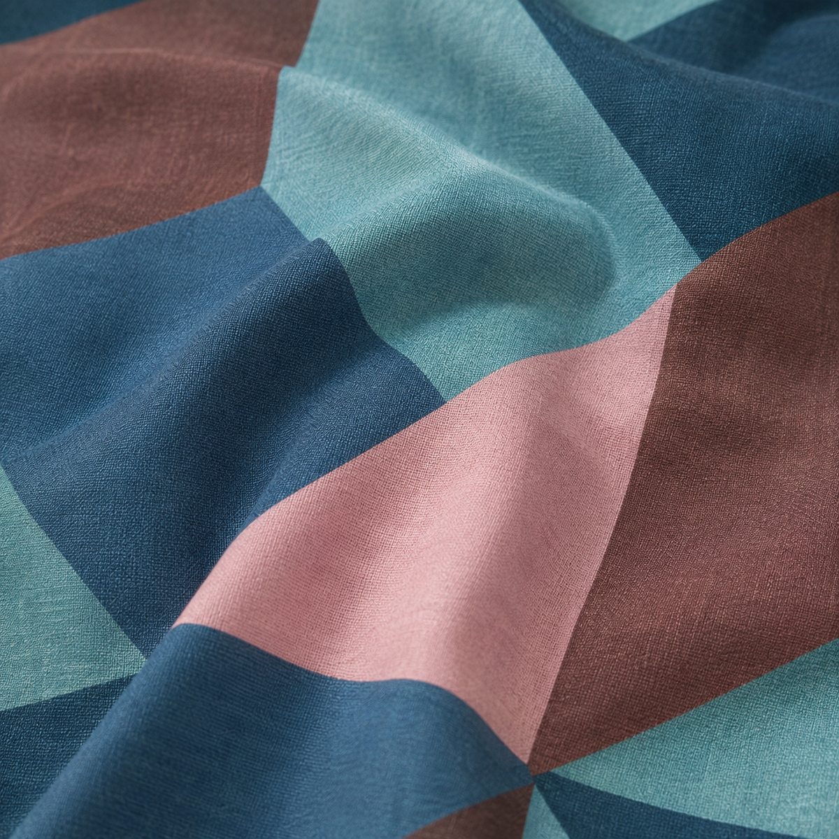 A close-up of draped fabric with a geometric color-block pattern in dusty pink, teal, slate blue, and brown.